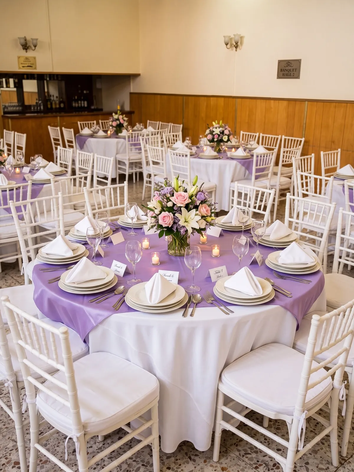 Salón de banquetes con mantelería lila y centro floral rosa