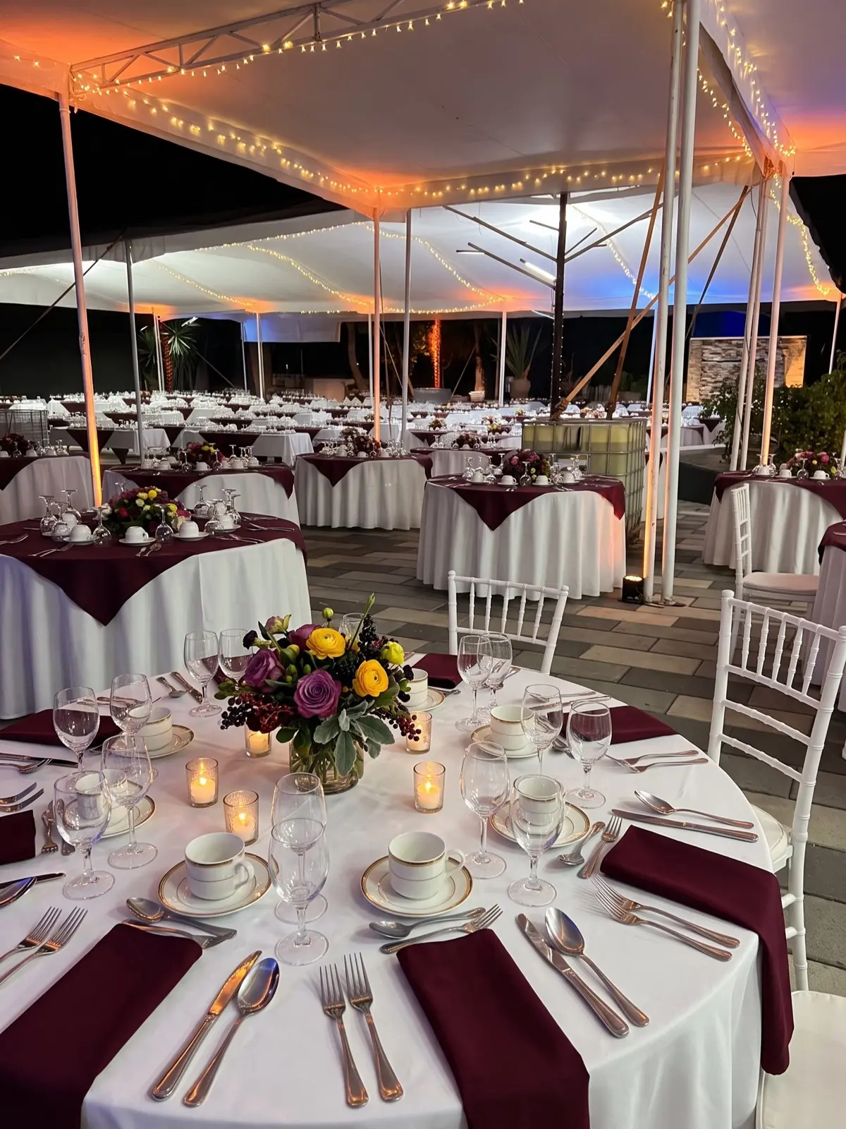Carpa nocturna con mesas vestidas en blanco y vino tinto